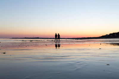 Silhouette couple walking on shore beach against sky during sunset