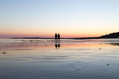 Silhouette people on beach against clear sky during sunset