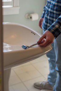 Low section of man holding razor while standing in bathroom