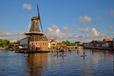 Paddleboarders passing the windmill on the river de spaarne on a clear day. haarlem, the netherlands
