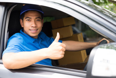 Man with packages gesturing thumbs cup while sitting in car seen through window