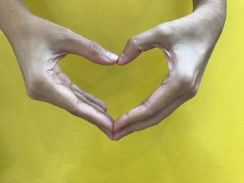 Cropped hands forming heart shape on yellow table