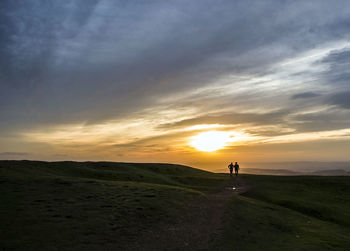 People walking on landscape against sky during sunset