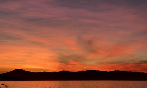 Scenic view of dramatic sky over silhouette mountains during sunset