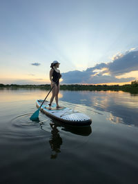 Rear view of woman swimming in sea against sky during sunset