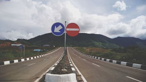 Road sign by street against sky