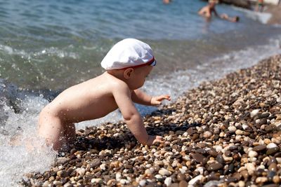 Side view of shirtless baby crawling on shore