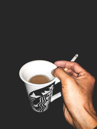 Close-up of hand holding coffee cup against black background