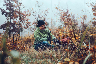 Woman with backpack having break during autumn trip drinking a hot drink from thermos flask