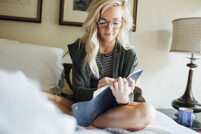 Woman writing diary while sitting on bed at home