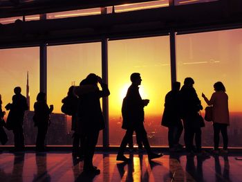 People in glass building against sky during sunset