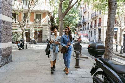 Female friends talking while walking on sidewalk in city