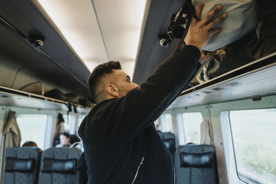 Side view of man loading luggage on shelf in train