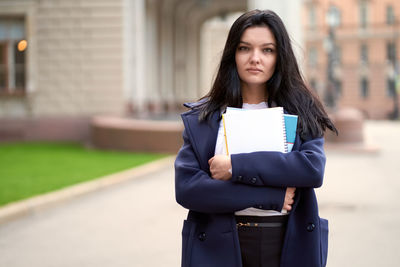 Portrait of young woman holding books outside university