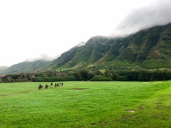 People riding horse on field against mountains