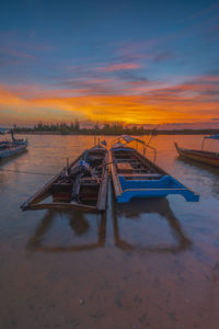 Boat moored on shore against sky during sunset