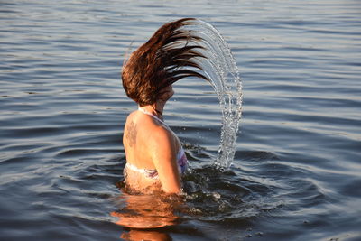 Side view of woman splashing water from hair in lake
