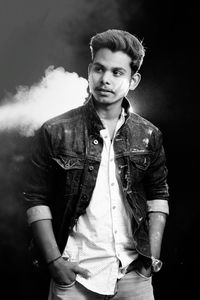 Portrait of young man standing against black background