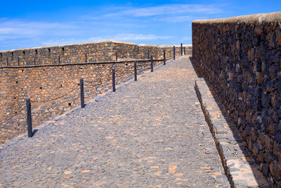 Footpath by wall against sky