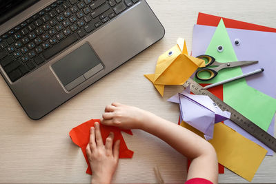 Cropped hand of girl doing origami on table