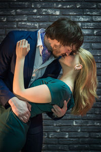 Affectionate couple kissing while standing against wall