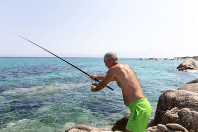 Fisherman sitting on a rock and fishing with a rod