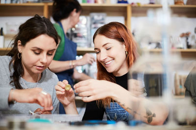 Smiling young female engineer holding electrical component by colleague at workshop