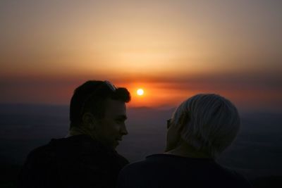 Couple talking against orange sky during sunset