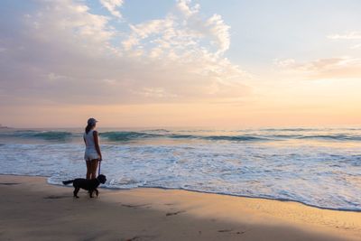 Woman standing with dog at beach against sky