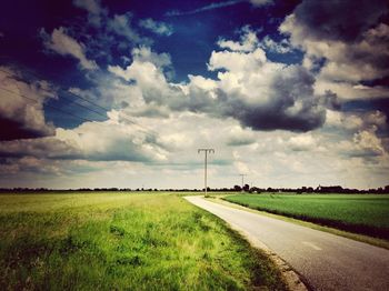 Road passing through field against cloudy sky