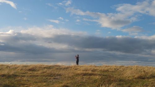 Mid distance of man standing on grassy field against cloudy sky