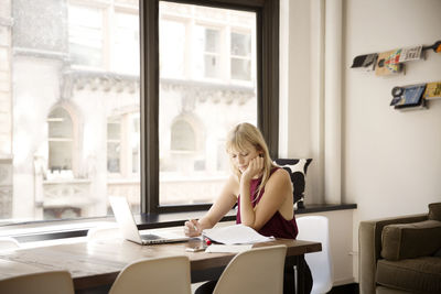 Businesswoman reading file at desk by window in creative office