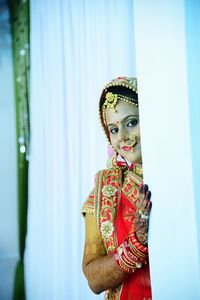 Close-up portrait of bride in sari standing against curtain