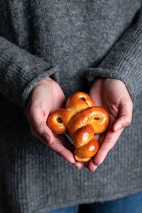 Crop female in cozy gray sweater and jeans holding traditional fresh baked saffron buns with raisin and sprinkles