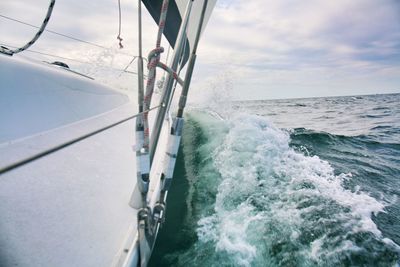 Water splashing by sailboat sailing on sea against sky