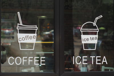 Close-up of text and disposable cups on door of cafe