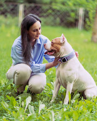 Young woman squatting and petting american pitbull terrier in park. happy dog with tongue out