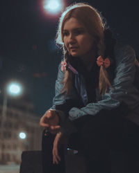 Young woman looking at illuminated camera at night