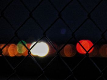 Defocused image of illuminated chainlink fence against sky at night