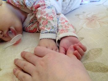 Cropped hand by baby sleeping on bed at home