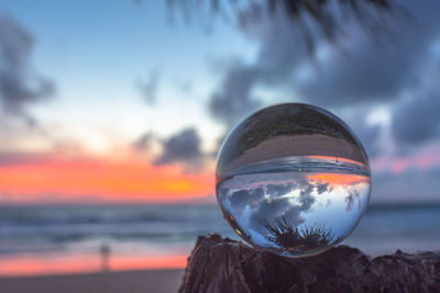 Close-up of crystal ball on sea against sky during sunset