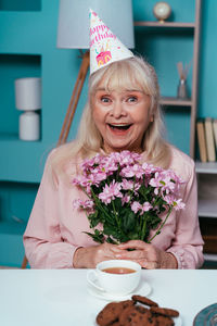 Portrait of smiling senior woman holding flowers at home