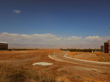 Road passing through field against sky