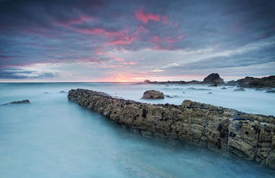 Scenic view of sea against cloudy sky during sunset