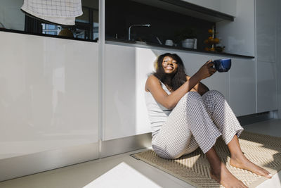 Happy woman sitting with tea cup in kitchen at home