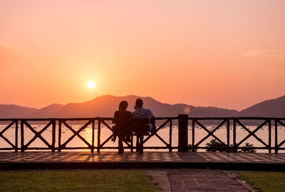 Men standing on railing against sky during sunset