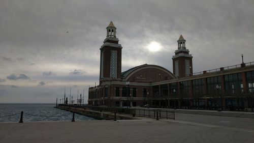 Buildings by sea against cloudy sky