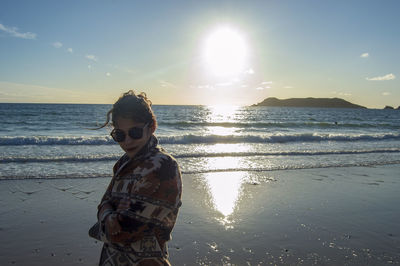 Woman standing at beach against sky during sunset