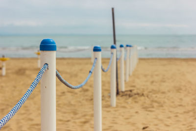 Bollards at beach against cloudy sky