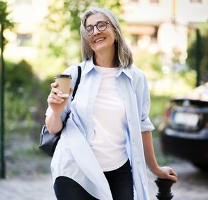 Happy mature woman enjoying a cup of coffee on a summer day while sitting outdoors on a city street.